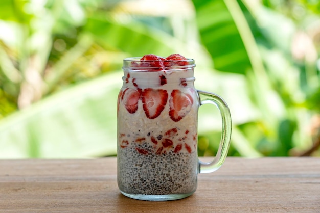 Pudding de chia au lait d'amande avec des fraises rouges fraîches, des baies de goji et des flocons d'avoine dans une tasse en verre