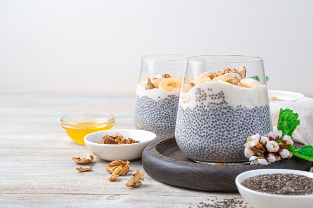 Pudding naturel, riche en vitamines, calcium et oméga 3 avec graines de chia, noix et miel sur un mur en bois clair. Vue latérale, copiez l'espace.