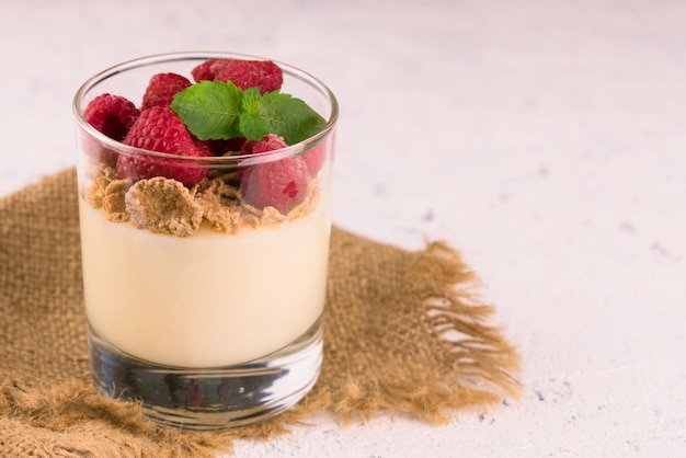 Pudding à la vanille avec des framboises dans un verre sur une plaque blanche Gros plan