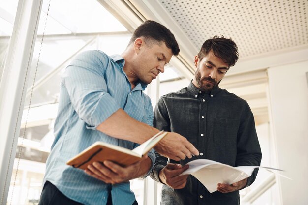 Puis-je jeter un coup d'œil à cette photo rapidement recadrée de deux beaux jeunes hommes d'affaires regardant leurs notes après une réunion réussie dans la salle de conférence