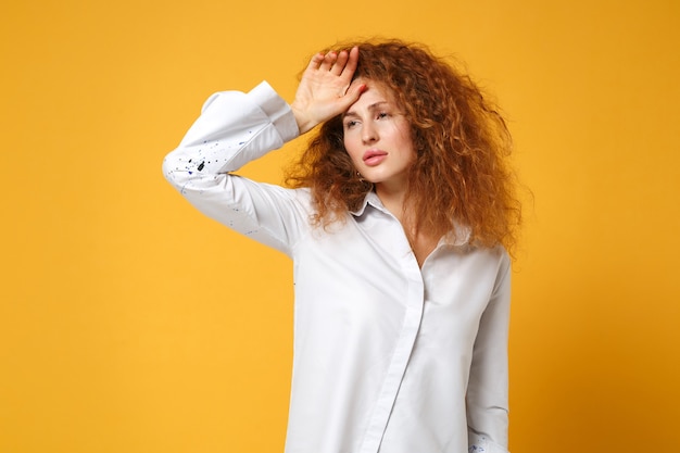 Épuisé fatigué jeune femme rousse fille en chemise blanche posant isolé sur mur jaune orange