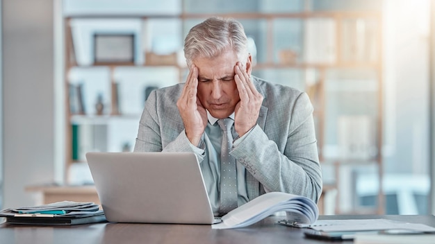 Épuisement de stress et homme d'affaires senior avec un mal de tête problème d'affaires et crise sur un ordinateur portable Santé mentale employé fatigué et mature avec une migraine mauvaise nouvelle et douleur d'un délai de travail