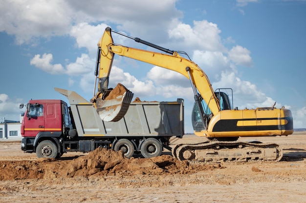 Une puissante pelle sur chenilles charge la terre dans un camion-benne contre le ciel bleu Développement et enlèvement du sol du chantier de construction