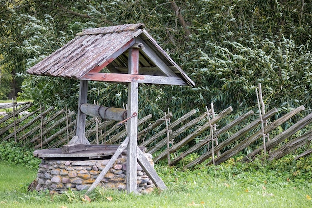 un puits d'eau en bois avec un toit et une clôture en bois de osier derrière