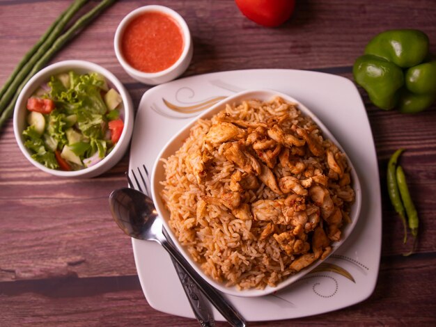 Pulao de poulet indien épicé avec sauce à salade et cuillère dans un plat vue de dessus sur fond de bois