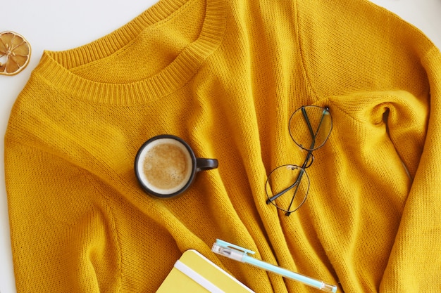 Pull jaune vif avec bloc-notes, stylo, lunettes et une tasse de café