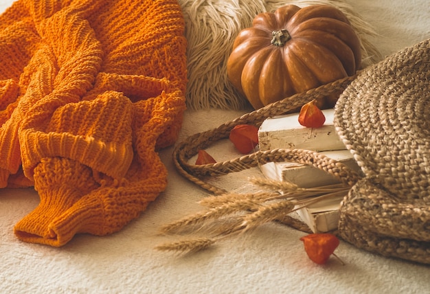 Pull orange chaud tricoté confortable avec de vieux livres et sac de paille vintage sur plaid chaud blanc avec citrouille, physalis, livres d'automne et lecture. humeur d'automne. Heure d'automne d'hiver.