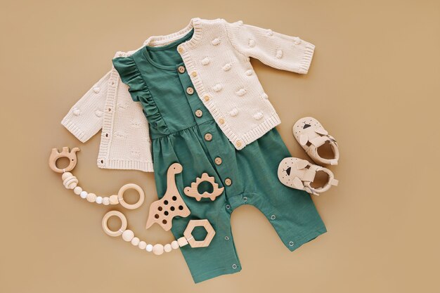 Pull en tricot avec barboteuse verte, jouets en bois et chaussures de bébé. Ensemble de vêtements et accessoires de bébé pour petite fille sur fond beige. Nouveau-né de mode. Mise à plat, vue de dessus