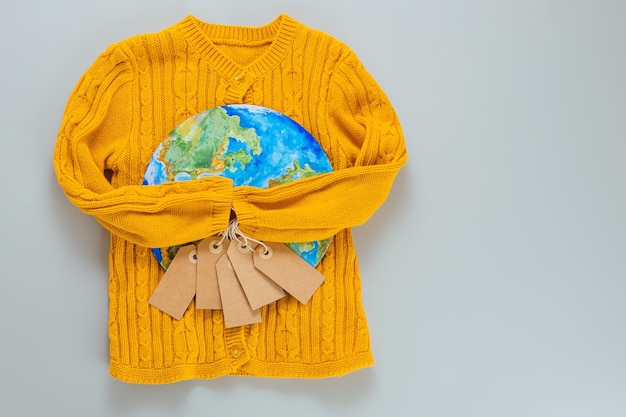 Un pull en tricot jaune avec une planète Terre peinte sur fond gris. Achetez moins