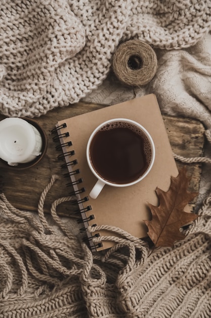 Pulls et tasse de thé avec cahier, bougie et vêtements à tricoter