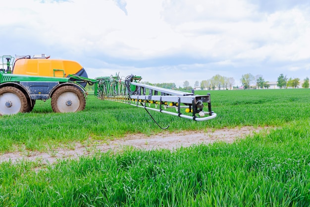 Pulvérisation de pesticides sur de jeunes blés au champ à l'aide d'un pulvérisateur tracteur.