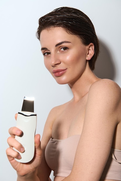 Épurateur de cosmétologie à ultrasons. Procédure de cavitation faciale. Soins de la peau en salon. Matériel d'épluchage professionnel. Jolie femme traitant son visage avec un équipement de spa électrique. Copier l'espace publicitaire