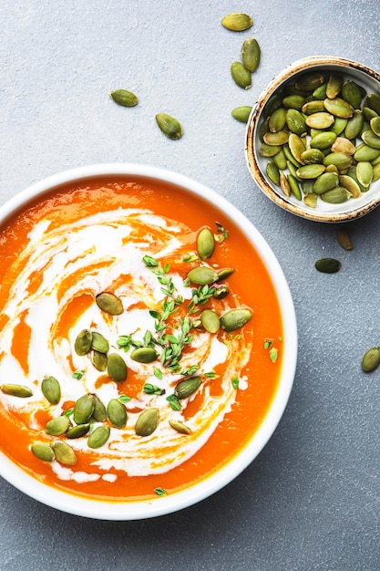 Purée de soupe crémeuse à la citrouille avec crème de graines de citrouille et thym Hiver ou automne nourriture lente végétarienne saine Bol de soupe blanche sur fond de table gris Vue de dessus