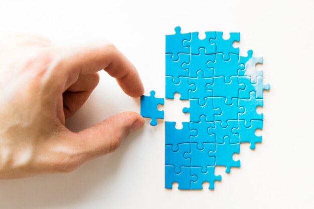Puzzle bleu à la main. Main tenant la pièce du puzzle sur fond blanc. Pièce jointe puzzle, connexion d'affaires, éducation, société et travail d'équipe