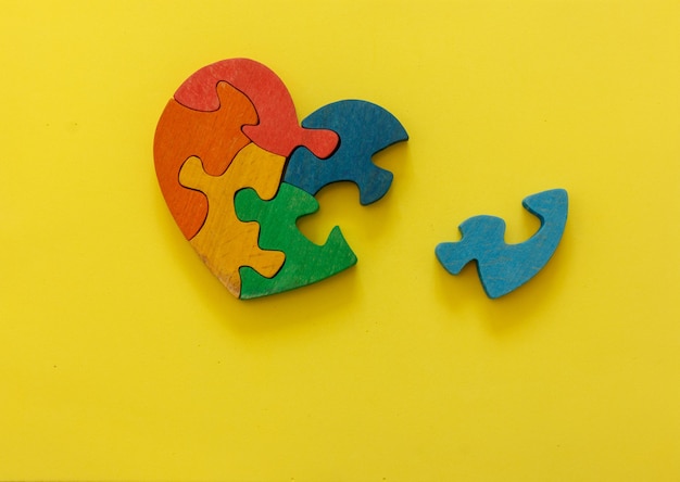 Puzzle multicolore en bois en forme de coeur sur fond jaune. Concept Saint Valentin, relation. Espace pour le texte