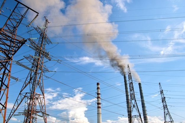 Pylônes électriques à haute tension contre les tuyaux hauts de la centrale au charbon avec de la fumée noire se déplaçant vers le haut, une atmosphère polluante. Production d'énergie électrique avec le concept de combustible fossile