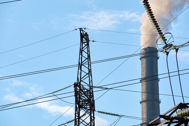 Pylônes électriques à haute tension contre les tuyaux hauts de la centrale au charbon avec de la fumée noire se déplaçant vers le haut, une atmosphère polluante. Production d'énergie électrique avec le concept de combustible fossile.