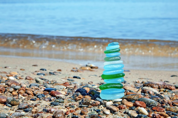 Pyramide équilibrée de fragments de bouteilles en verre polis par la mer dans le contexte de la vague venant en sens inverse