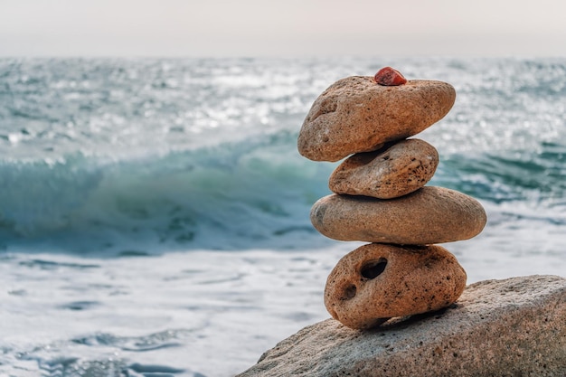 Pyramide de galets équilibrée sur la plage par une journée ensoleillée Écume de mer sur le fond Mise au point sélective Pierres zen sur la mer plage méditation spa harmonie calme équilibre concept