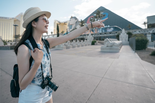 pyramide et sphinx à Las Vegas Nevada. joyeuse jeune fille backpacker portant un appareil photo vintage à la recherche de la direction de l'attraction touristique. vue latérale d'une femme asiatique excitée pointant du doigt le voyageur