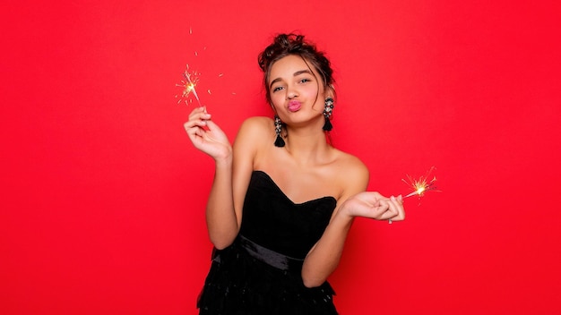 Pyrotechnie et concept de personnes souriante jeune femme ou adolescente femme heureuse avec des cierges magiques célèbrent en robe noire sur fond rouge fille souriant aux lèvres de la caméra avec une paille