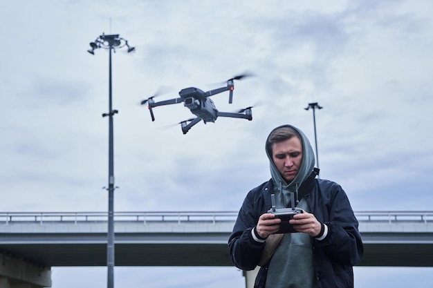 Quadcopter vidéographie jeune homme tient un panneau de commande avec moniteur dans sa main tourne une vidéo d'un paysage urbain