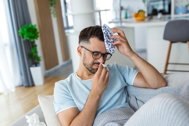 Quand vous frappez une étagère avec votre tête Jeune homme frustré tenant un sac de glace sur la tête allongé sur le canapé à la maison