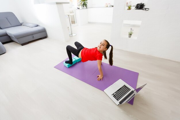 Quarantaine à la maison. petite fille faisant du yoga en ligne sur un ordinateur portable pendant la quarantaine d'auto-isolement