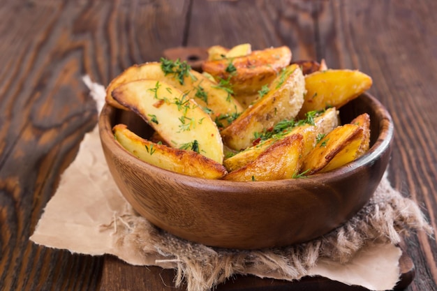 Quartiers de pommes de terre à l'aneth dans un bol en bois sur fond de bois