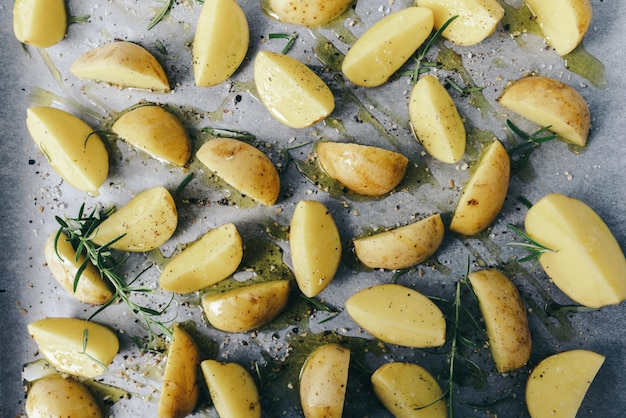 quartiers de pommes de terre crues avec de l'huile et du poivre sur une plaque de cuisson, fond de concept alimentaire