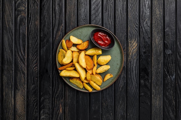 Quartiers de pommes de terre frites servies avec une sauce tomate au ketchup tirée d'en haut sur une table en bois