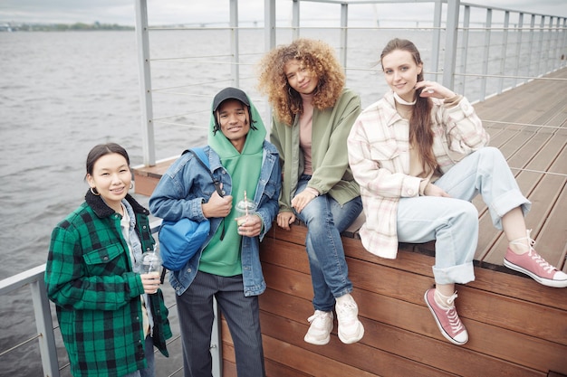 Photo quatre adolescents heureux en tenue décontractée reposant sur une jetée en bois le week-end