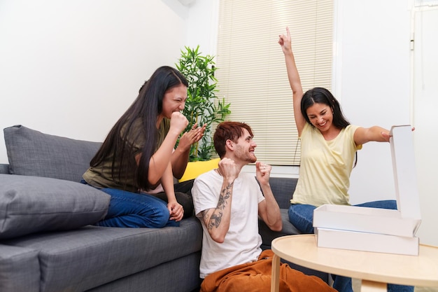 Quatre amis expriment leur triomphe et leur joie dans leur appartement en célébrant avec de la pizza.