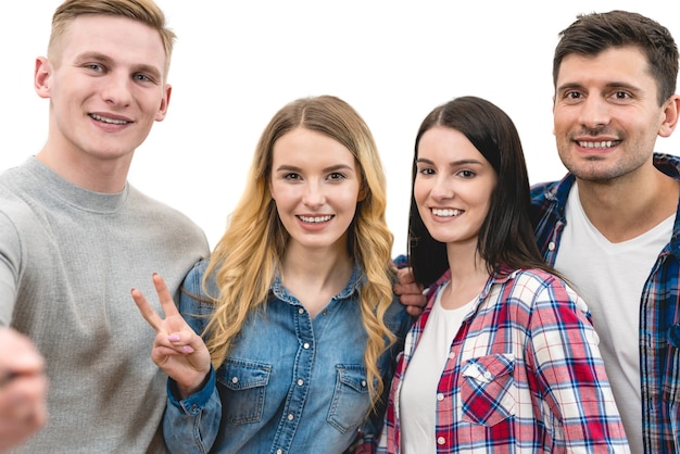 Les quatre amis heureux font un selfie de portrait sur le fond blanc