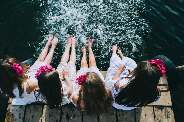 Quatre amis de jeunes filles assis sur un jet avec les jambes pendantes à l&#39;eau un jour d&#39;été