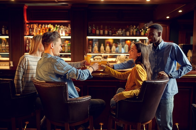 Quatre amis joyeux boivent de la bière au comptoir du bar. Groupe de personnes se détendre dans un pub, mode de vie nocturne, amitié, célébration de l'événement