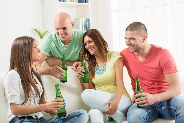 Quatre amis s'amusant avec de la bière ensemble à la fête à la maison.