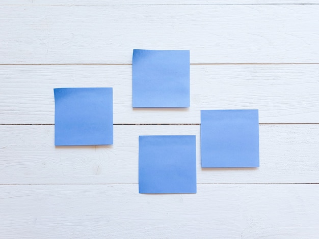 Quatre autocollants en papier bleu sur un mur de planche de bois blanc.