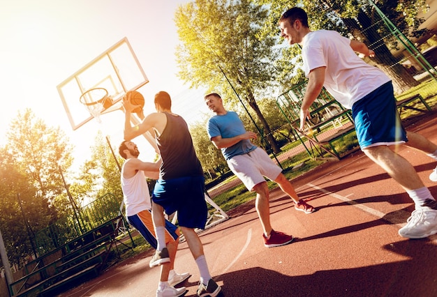 Quatre basketteurs s'entraînent en plein air. Ils jouent et agissent ensemble.