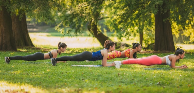 Quatre belles amies faisant de l'exercice de planche dans le parc.