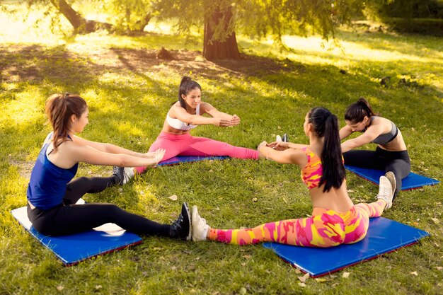 Quatre belles amies faisant des exercices d'étirement dans le parc. Mise au point sélective.