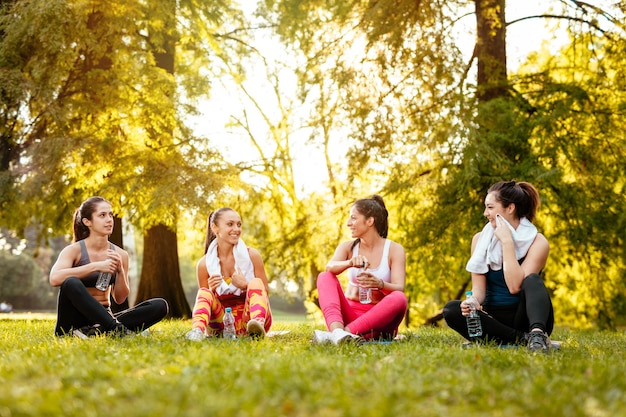 Quatre belles amies motivées se détendent après s'être entraînées dans le parc de la ville.