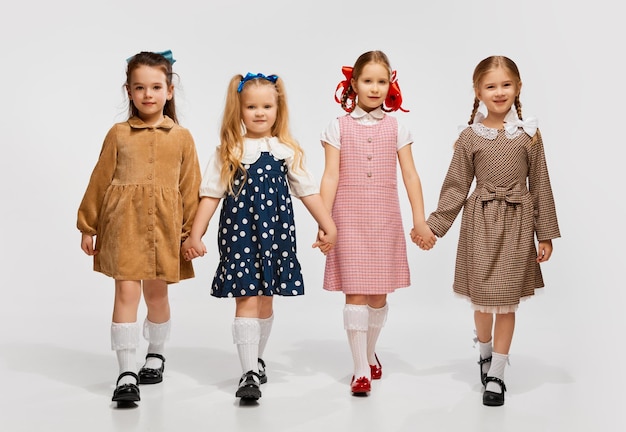 Quatre belles petites filles enfants dans des robes rétro élégantes posant marchant contre un studio gris