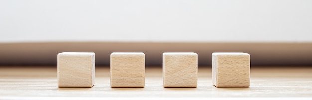 Quatre blocs de bois carrés sont disposés sur la table. Un bloc de bois avec un espace de copie pour le texte ou les symboles est utilisé pour faire des bannières. Fond de bannière panoramique avec espace de copie.