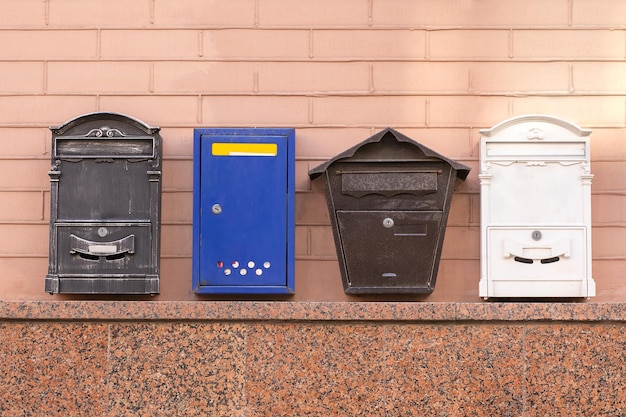 Quatre boîtes aux lettres de différentes formes et couleurs accrochées à un mur de briques dans une zone urbaine