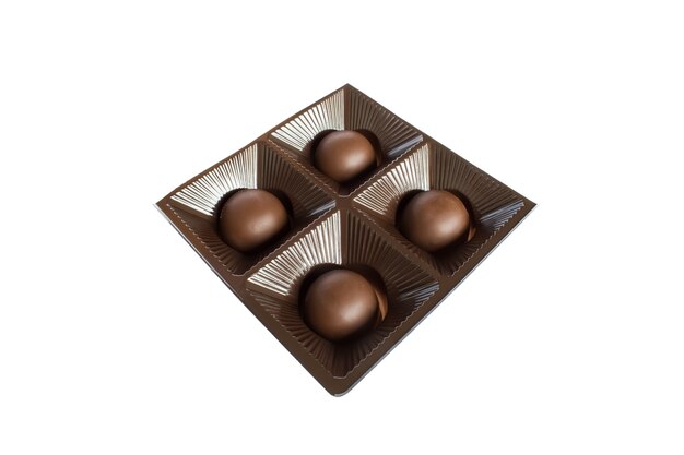 Quatre bonbons au chocolat rond dans un emballage carré en plastique sur un mur blanc