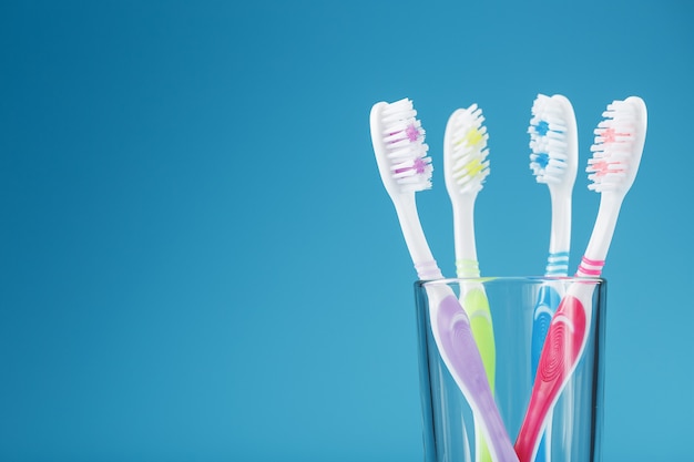 Quatre brosses à dents dans un verre sur une surface bleue