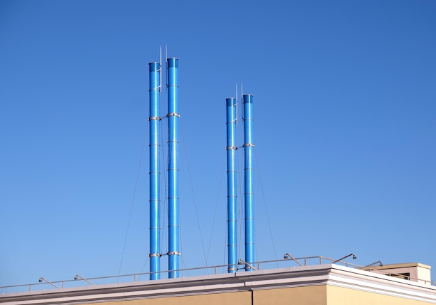 Quatre cheminées de fumée peintes en bleu après le toit du bâtiment sur un ciel bleu clair sans nuages