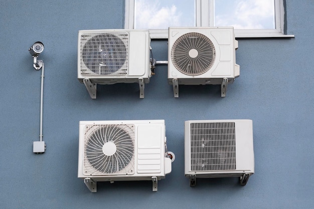 Quatre climatiseurs et une caméra CCTV fixés au mur à l'extérieur du bâtiment pendant la journée