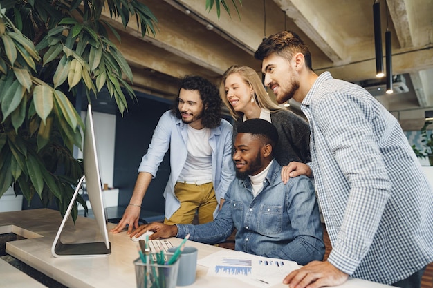 Photo quatre collègues multiethniques regardant un écran d'ordinateur au bureau